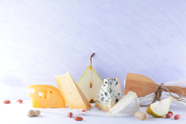 Various cheeses, pears and peanuts on white background. Blue cheese and camembert on parchment paper. Dairy products and fruits for breakfast. Healthy food - Foto, imagen