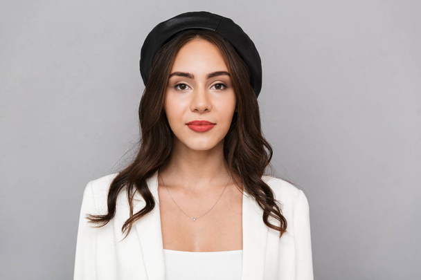 Portrait of a beautiful young woman wearing beret standing isolated over gray background, looking at camera - Foto, Bild