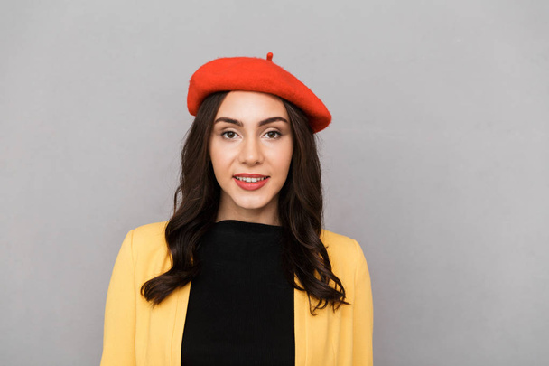 Close up of a smiling young woman in red hat standing over gray background, looking at camera - Foto, afbeelding
