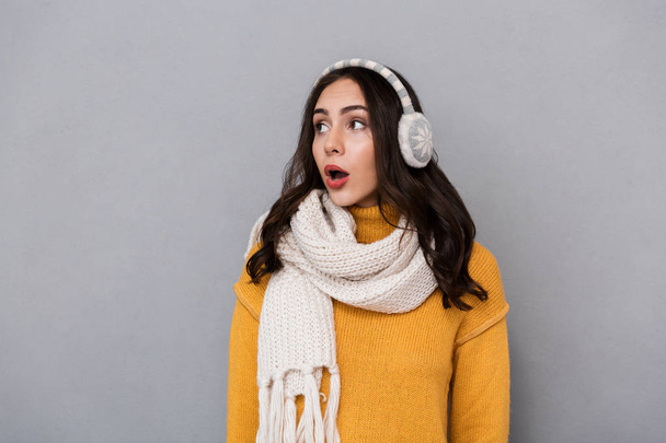 Portrait of a shocked young woman wearing sweater and scarf isolated over gray background - Foto, Bild