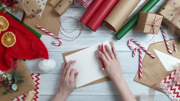 Női tini kézzel írt levélben Santa ajándék, fából készült tábla, csomagoló papír, piros karácsonyi díszek. Karácsonyt és boldog új évet összetétele. Lapos feküdt, top view - Felvétel, videó
