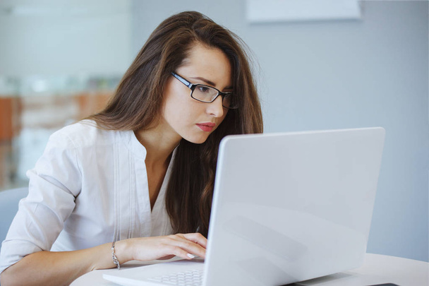 Businesswoman in a glasses and white blouse sits at a table with a laptop in the office and solves the problem. Gender equality. Good deal. Attentive look and focus. Female leadership. - Photo, Image