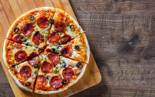 Pizza Mozzarella peyniri, sucuk, domates, biber, zeytin, salam. Ahşap masa arka plan üzerinde İtalyan pizza - Fotoğraf, Görsel