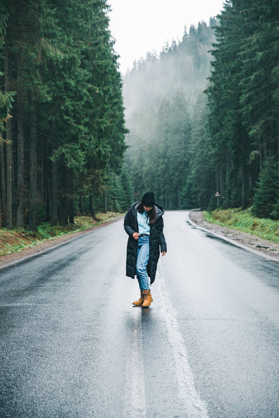 Nuori nainen seisoo keskellä tietä talvella vuoristossa metsä. matkustuskäsite
 - Valokuva, kuva