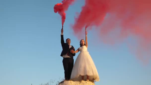 Ευτυχισμένη νύφη και τον γαμπρό κουνώντας το κόκκινο χρώμα που καπνίζουν κατά της μπλε του ουρανού. - Πλάνα, βίντεο