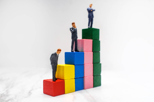 Uomini d'affari in miniatura si trovano su blocchi di legno che simboleggiano passi verso il successo
 - Foto, immagini