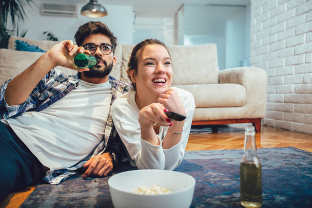 Happy νεαρό ζευγάρι χαλαρωτικό και βλέποντας τηλεόραση στο σπίτι - Φωτογραφία, εικόνα