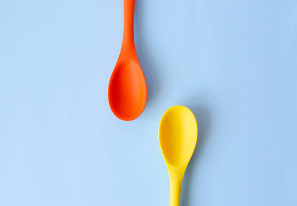Two silicone colored large spoons of yellow and orange on a blue background. - 写真・画像