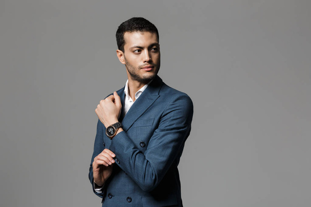 Image of successful arabic businessman 30s in formal suit looking aside and demonstrating wristwatch isolated over gray background - Foto, Imagem