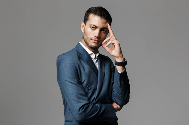 Image of successful arabic businessman 30s in formal suit thinking and holding index finger at forehead isolated over gray background - Foto, Imagem