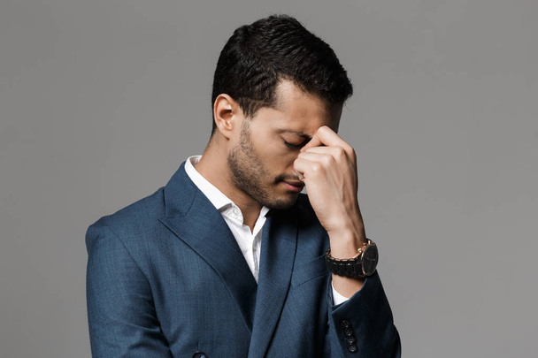 Image of a sad tired business man with headache posing isolated over grey wall background. - Φωτογραφία, εικόνα
