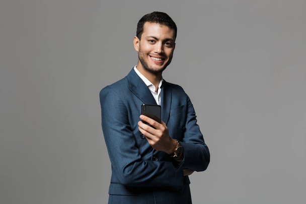 Image of handsome business man holding mobile phone posing isolated over grey wall background. - Fotografie, Obrázek