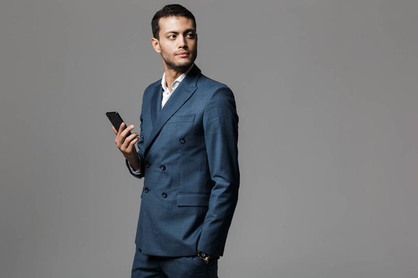 Image of a handsome young business man isolated over grey wall background using mobile phone. - Foto, afbeelding