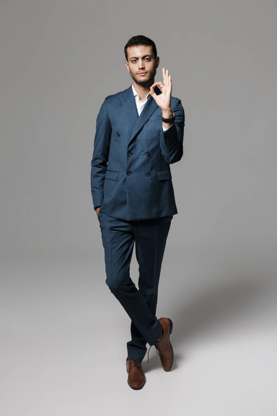 Full length image of positive arabic businessman 30s in formal suit gesturing at camera isolated over gray background - Zdjęcie, obraz
