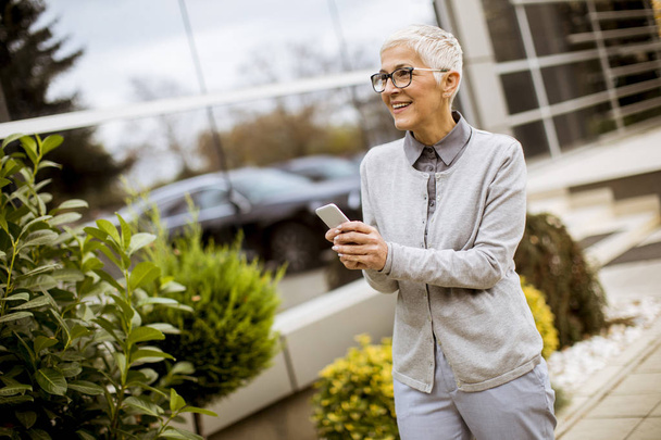 S úsměvem vedoucí podnikatelka mluvit na telefonu, zatímco ona stojí před kancelářská budova - Fotografie, Obrázek