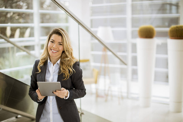 Vrolijke jonge zakenvrouw met tablet in het moderne kantoor - Foto, afbeelding