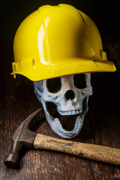 Menselijke schedel met bouw werknemer harde hoed met hamer symboliseert de gevaren van deze lijn van het werk - Foto, afbeelding