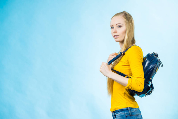 Blonde teenage girl going to school or college wearing stylish backpack. Outfit trendy accessories. On blue - 写真・画像
