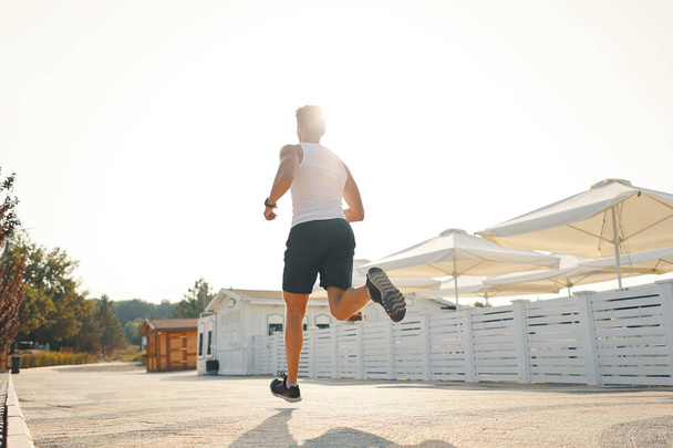 Pełna długość strzał zdrowy młody człowiek działa na promenadzie w godzinach porannych. Mężczyzna runner Sprint na zewnątrz. - Zdjęcie, obraz