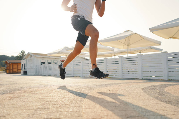 Nahaufnahme der Beine eines Stadtläufers, der auf der Straße läuft, sonniger Tag Hintergrund, Abwinkelung. Konzept für einen gesunden Morgen. - Foto, Bild