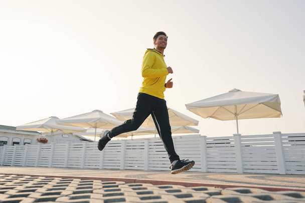 Повнометражний знімок здорового молодого чоловіка, що біжить на набережній вранці. Чоловік бігун біжить на відкритому повітрі. Кут вниз
 - Фото, зображення