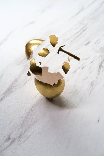 Martelo minúsculo quebra ovo dourado com ação pedaços de concha quebrados
 - Foto, Imagem