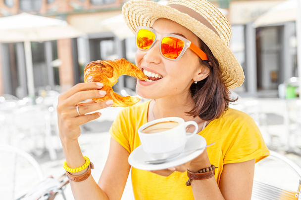 Счастливая женщина в желтом, завтракающая круассанами и кофе в открытом кафе
 - Фото, изображение