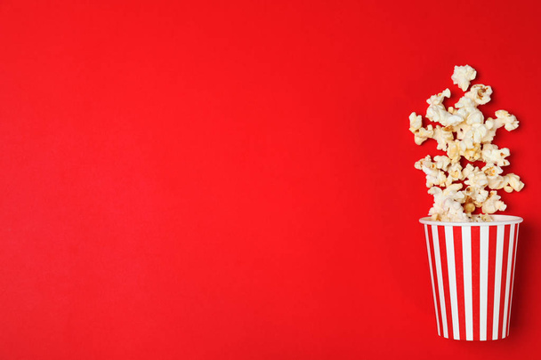 Overturned paper cup with tasty popcorn on color background, top view. Space for text - Foto, imagen