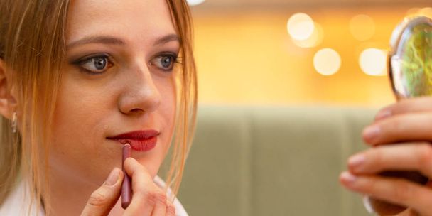 Girl office manager in a business blouse paints her lips and makes make-up during a coffee break in the office. - Foto, Bild
