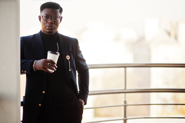 Fashionable african american man in suit and glasses with cup of coffee at hands posed on balkony at office. - Foto, Imagen