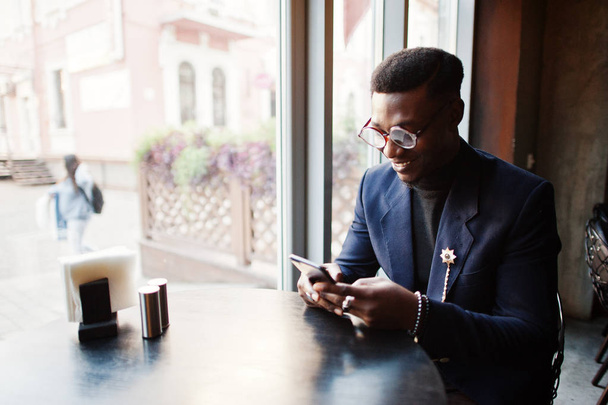 Fashionable african american man in suit and glasses holding mobile phone at hands posed on cafe. - Photo, image
