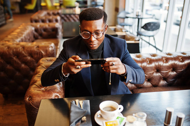 Divatos afroamerikai férfi öltöny és telefon kávézó és a snap kávé ül szemüveg. - Fotó, kép