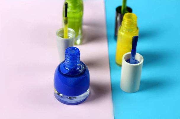 Blue and green nail lacquer bottles and nail brushes on blue and pink background - Photo, Image