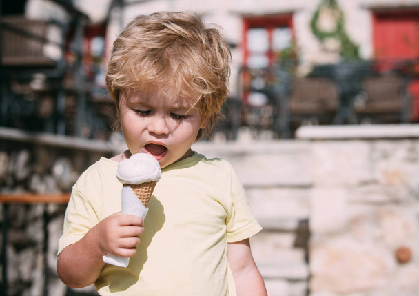 Aranyos fiú kezében fagylalttal. Szőke fiú eszik fehér fagylalt kúpot. Forró nyár, ideje édes fagylalt. Nyári időszámítás járni a gyermek. Gyerek nyaralni a meleg napsütésben. Finom hideg desszert - Fotó, kép