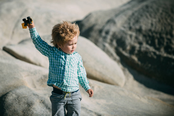 Junge, der mit Spielzeugauto Hand in Hand auf Felsen am Meer spielt. Nette nachdenkliche Kind geht und ein starker Wind weht in seinen Haaren. Wandern wie gesundes Wachstum. Transport in der Wüste - Foto, Bild