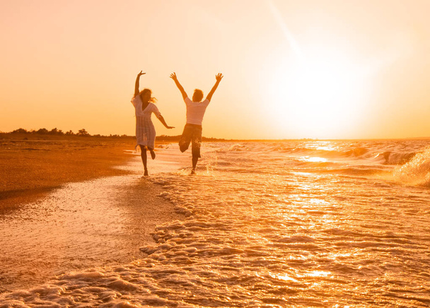 boldog pár fut a parton naplementekor - Fotó, kép