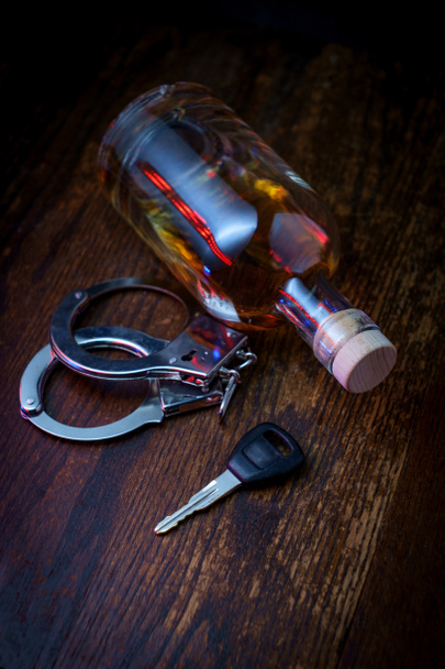 Une bouteille de whisky à moitié vide sur un bar rustique en bois avec des clés et des menottes symbolisant l'arrestation pour conduite en état d'ébriété - Photo, image
