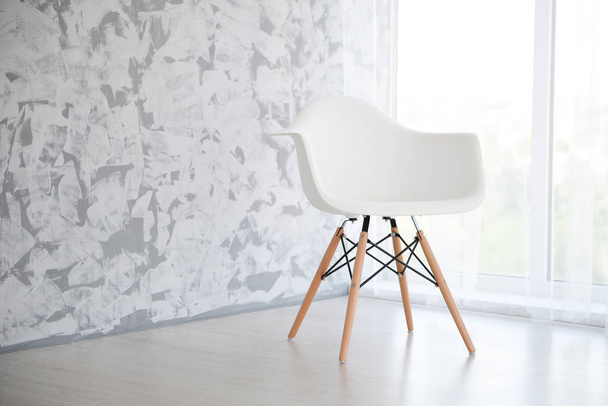 egy fehér szék egy világos szobában egy szürke falnak támasztva az ablakhoz közel - Fotó, kép