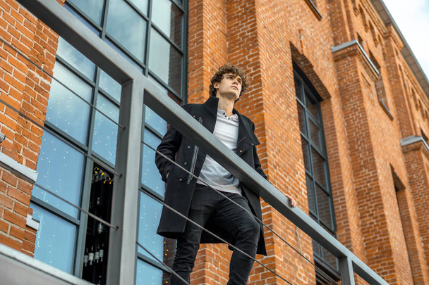 Attractive pensive man standing on staircase on red bricked building background. - Foto, imagen