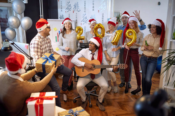 Χαρούμενη επιχειρηματική ομάδα διασκεδάστε και χορέψτε στο Σάντα καπέλο στο Χριστουγεννιάτικο πάρτι στο γραφείο - Φωτογραφία, εικόνα