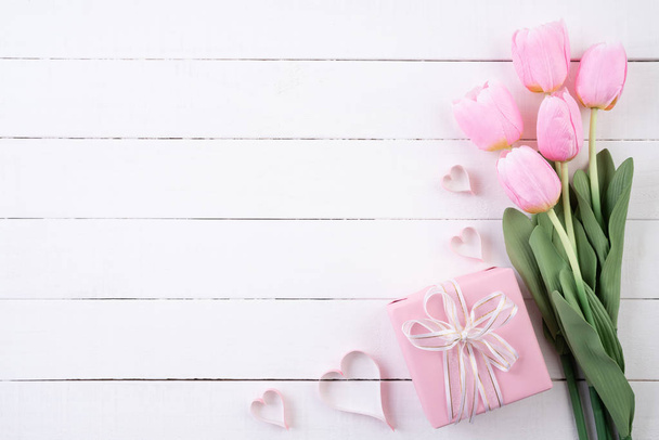 Valentines day and love concept. Pink paper hearts with gift box and tulips with ribbon on white wooden background. - Photo, image