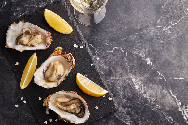 Huîtres sauvages néerlandaises servies avec des tranches de citron et du sel sur une table en marbre noir
 - Photo, image