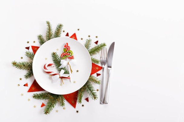 Elegant christmas table setting design captured from above top view, flat lay. Empty white plate, glass, cutlery, candy cane and decorations. - Photo, Image