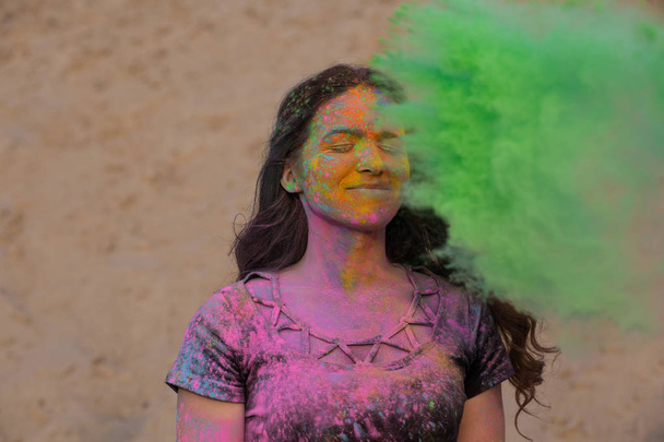 Magnífica mujer morena con el pelo largo ondulado divertirse con verde seco Holi polvo en el desierto
 - Foto, imagen