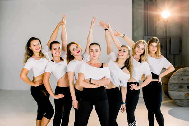 Happy young women standing together and smiling after exercising, holding arms up. Group of female friends relaxing after workout indoors. - Foto, Bild