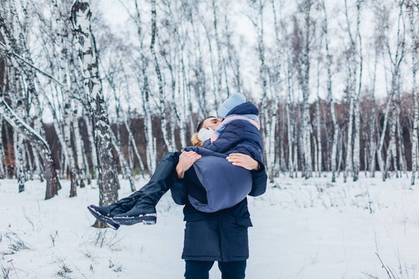 Guy carrying his girlfriend on hands in winter forest. Happy people having fun outdoors - Фото, зображення