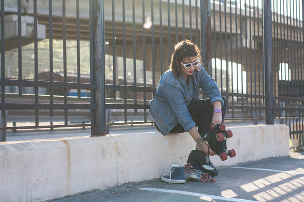 Stylish beautiful young woman in glasses and denim jacket rollerblading, dancing and having fun. Smiling and posing at sunset. Urban, rollers - 写真・画像
