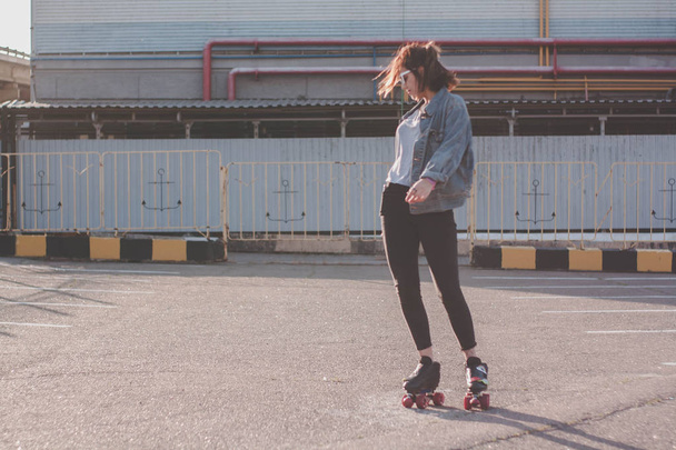 stylische junge Frau in Brille und Jeansjacke Rollschuh fahren, tanzen und Spaß haben. lächelnd und posierend bei Sonnenuntergang. Stadtverkehr, Roller - Foto, Bild