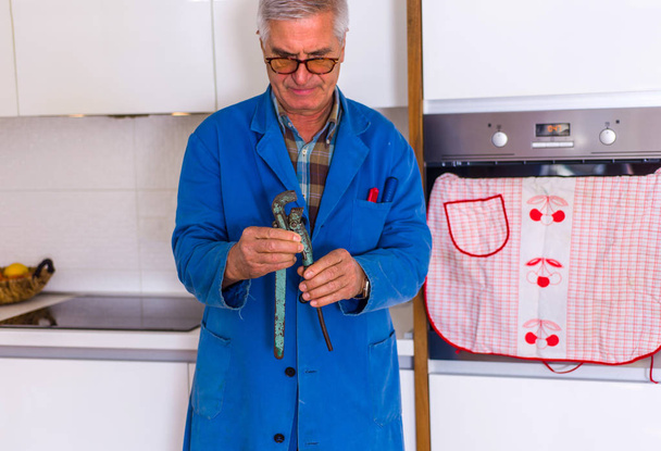 Пожилой мастер, стоящий на кухне и работающий с сварочными аппаратами
 - Фото, изображение