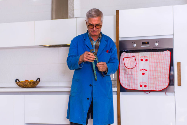 Old male repairman is holding his tools and working in the kitchen - Foto, afbeelding